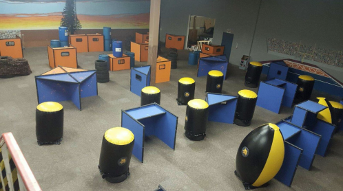 An indoor paintball arena featuring various colorful obstacles and structures for gameplay.