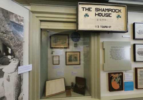 Display case featuring historical items related to The Shamrock House, with a sign and various framed pictures.