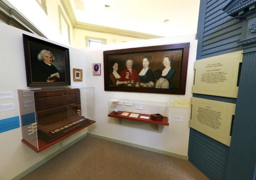 A museum exhibit featuring portraits, a keyboard instrument, and historical documents displayed on walls.