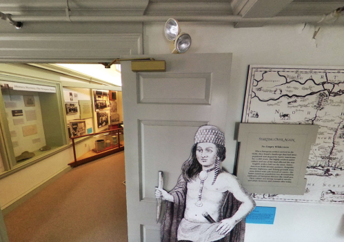 A historical exhibit featuring a doorway with a figure in traditional attire and informational displays in the background.