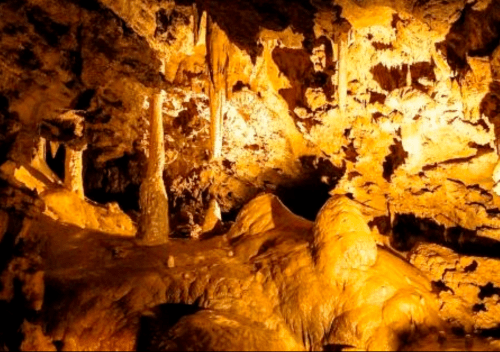 Stalactites and stalagmites illuminated in a warm-toned cave, showcasing unique rock formations.