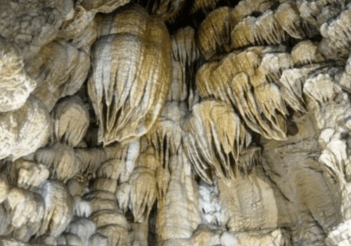 Stalactites and stalagmites create intricate formations on a cave wall, showcasing natural geological textures.