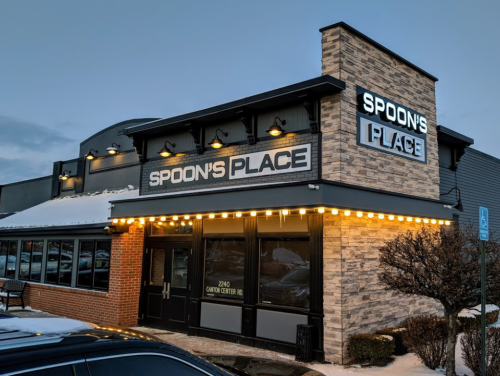 Exterior of Spoon's Place restaurant, featuring a stone facade and illuminated signage, with snow on the ground.