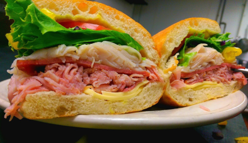 A close-up of a freshly cut sandwich with layers of turkey, ham, cheese, lettuce, and tomato on a crusty roll.