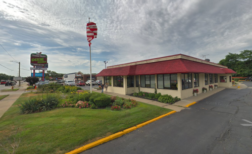 A restaurant with a red roof and flower beds, featuring an American flag and a sign in front.