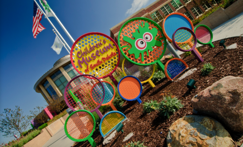 Colorful entrance sign for a children's museum, featuring playful designs and surrounded by greenery and rocks.