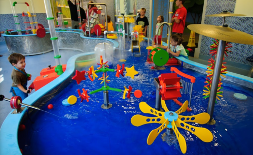 Children play in a colorful water play area with various interactive toys and water features.