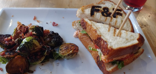 A toasted sandwich with F&F branding, served with roasted Brussels sprouts on a white plate.