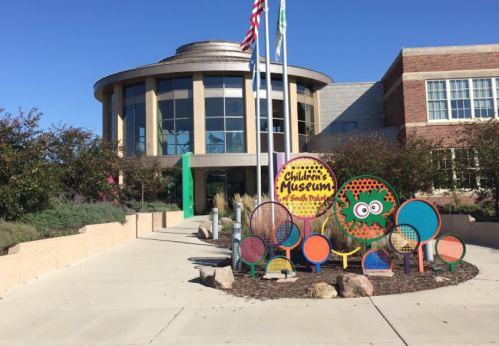 Exterior of a Children's Museum with colorful signage and playful decorations, surrounded by greenery and flags.