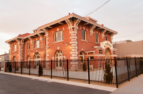 Historic brick building with arched windows and a decorative facade, surrounded by a black fence.