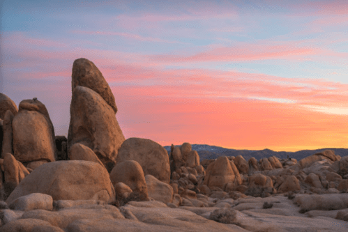 Rock formations under a colorful sunset sky in a desert landscape.