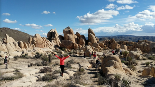 A group of people exploring a rocky landscape with large boulders under a blue sky with scattered clouds.