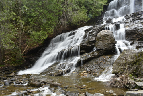A serene waterfall cascading over rocks, surrounded by lush green trees and a rocky riverbed.