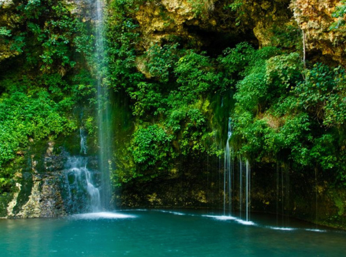 A serene waterfall cascading into a turquoise pool, surrounded by lush green foliage and rocky cliffs.
