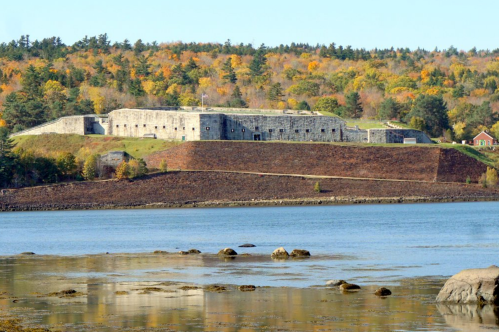 Historic stone fort on a hillside, surrounded by colorful autumn trees and a calm body of water in the foreground.