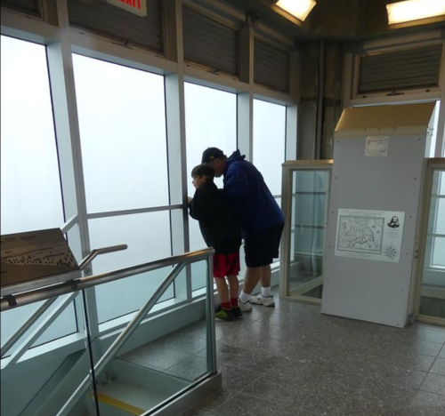 Two children look out a large window, with fog obscuring the view, in a modern observation area.