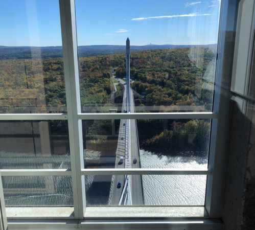 View of a bridge spanning a river, framed by large windows, with colorful autumn foliage in the background.