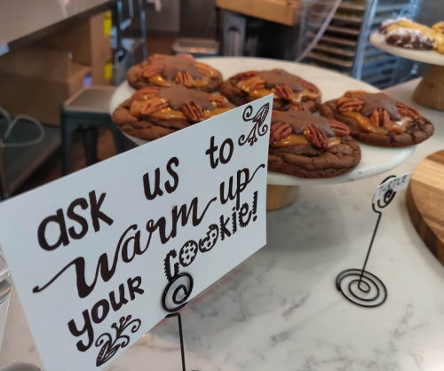 A display of cookies on a marble counter with a sign inviting customers to warm up their cookies.