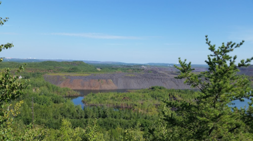 A scenic view of a landscape with a river, green trees, and a rocky hillside under a clear blue sky.