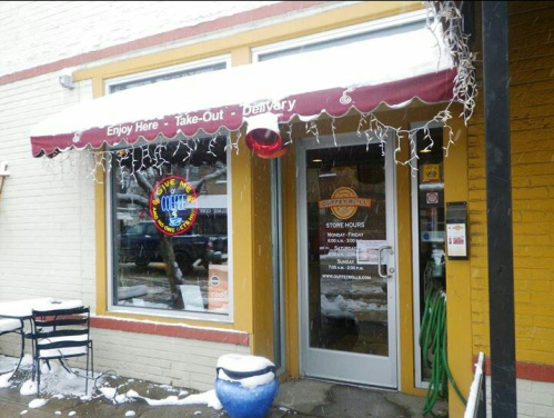 A cozy restaurant entrance with a red awning, snow on the ground, and festive lights hanging above the door.