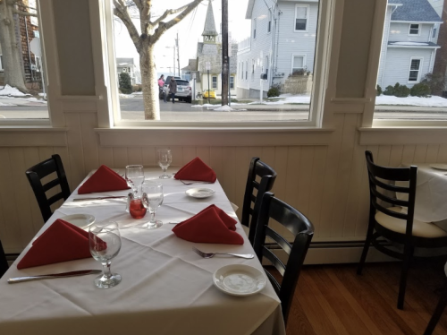 A dining table set with red napkins, glassware, and plates, with a view of a snowy street outside.