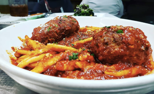 A bowl of pasta topped with meatballs and marinara sauce, garnished with herbs.