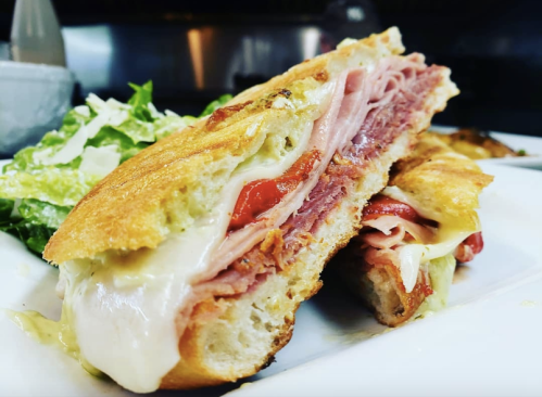 A close-up of a toasted sandwich filled with ham, cheese, and tomatoes, served with a side of lettuce.