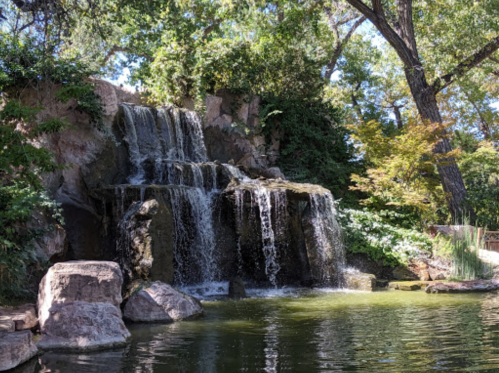 A serene waterfall cascading over rocks into a calm pond, surrounded by lush greenery and trees.