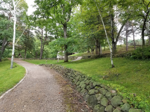 A winding gravel path surrounded by lush greenery and trees, leading through a peaceful park-like setting.