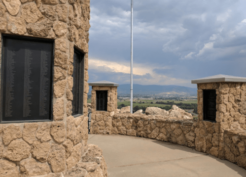 Stone structure with plaques on walls, overlooking a valley under a cloudy sky.