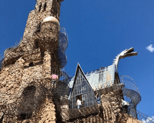 A whimsical stone structure with spiral staircases and a dragon sculpture against a clear blue sky.