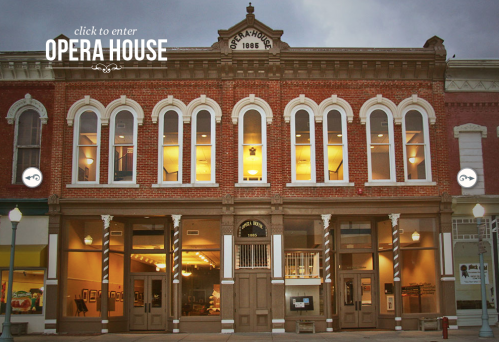 Historic Opera House building with a red brick facade, illuminated windows, and a "click to enter" sign.