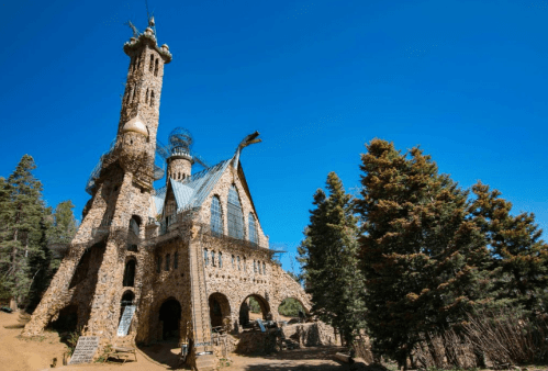 A whimsical stone castle with unique towers and a blue sky, surrounded by tall trees.