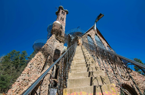 A unique stone tower with spiral staircases and a clear blue sky in the background, surrounded by trees.
