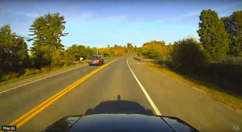 A scenic road curves through trees with autumn foliage, captured from a car's perspective.