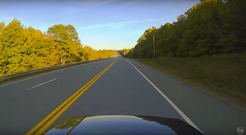 A scenic highway lined with trees in autumn colors under a clear blue sky.