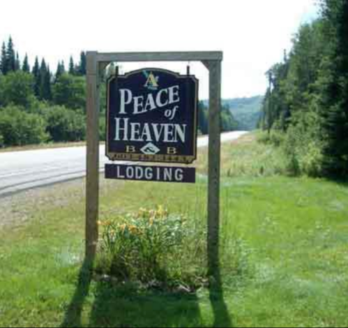 Sign for "At Peace of Heaven B&B" with "Lodging" below, surrounded by greenery along a roadside.