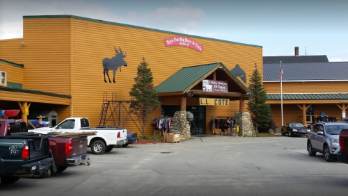 A rustic wooden building with a moose silhouette, featuring outdoor displays and parked trucks in front.