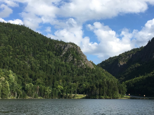 A serene lake surrounded by lush green mountains under a partly cloudy sky.