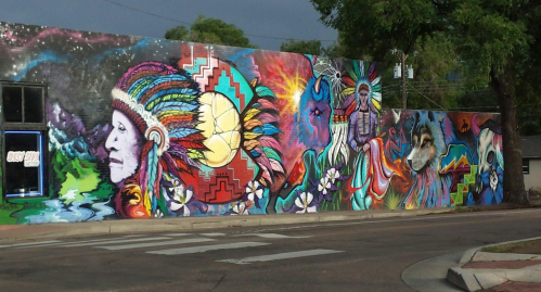 Colorful mural featuring Native American imagery, vibrant patterns, and nature elements on a city wall.