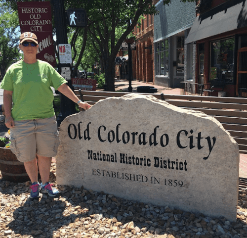 Person in a green shirt stands next to a stone sign for Old Colorado City National Historic District, established in 1859.