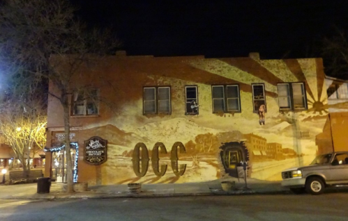 A building at night featuring a large mural with a desert landscape and the letters "OCC" prominently displayed.
