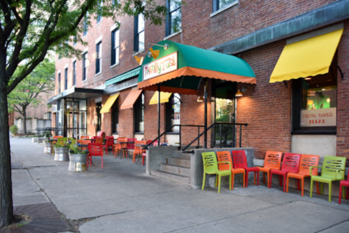 A colorful café exterior with orange and green awnings, featuring outdoor seating and a brick building backdrop.
