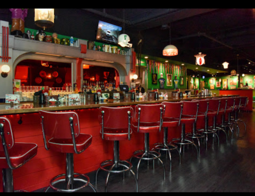A vibrant bar interior with red stools, green walls, and vintage decor, featuring a long counter and dim lighting.