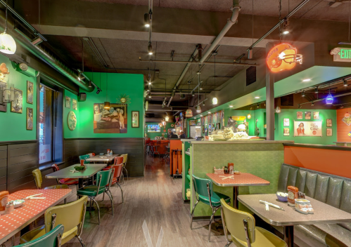 Colorful restaurant interior with green walls, retro decor, and empty tables set for dining. Warm, inviting atmosphere.