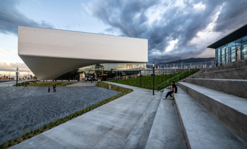Modern building of the U.S. Olympic & Paralympic Museum with cloudy skies and steps in the foreground.