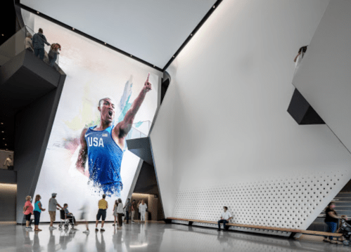 A modern interior featuring a large mural of an athlete in a blue USA uniform, with people observing and interacting.