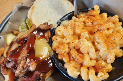 A plate featuring a BBQ chicken sandwich with cheese, pickles, and a side of creamy macaroni and cheese.