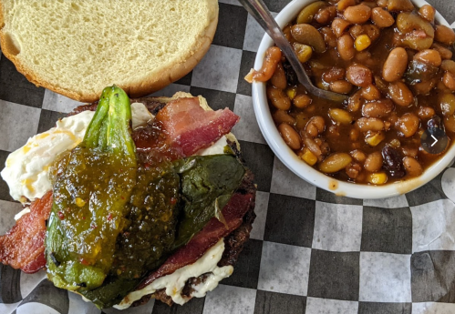 A sandwich with bacon, fried egg, and green peppers, served with a side of baked beans in a bowl.