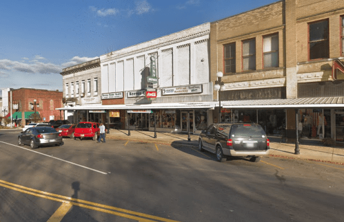 A street view of a small town with shops, parked cars, and a clear blue sky.